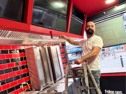Person streicht die rote Decke über der Grillstation, daneben die Dönerspieße